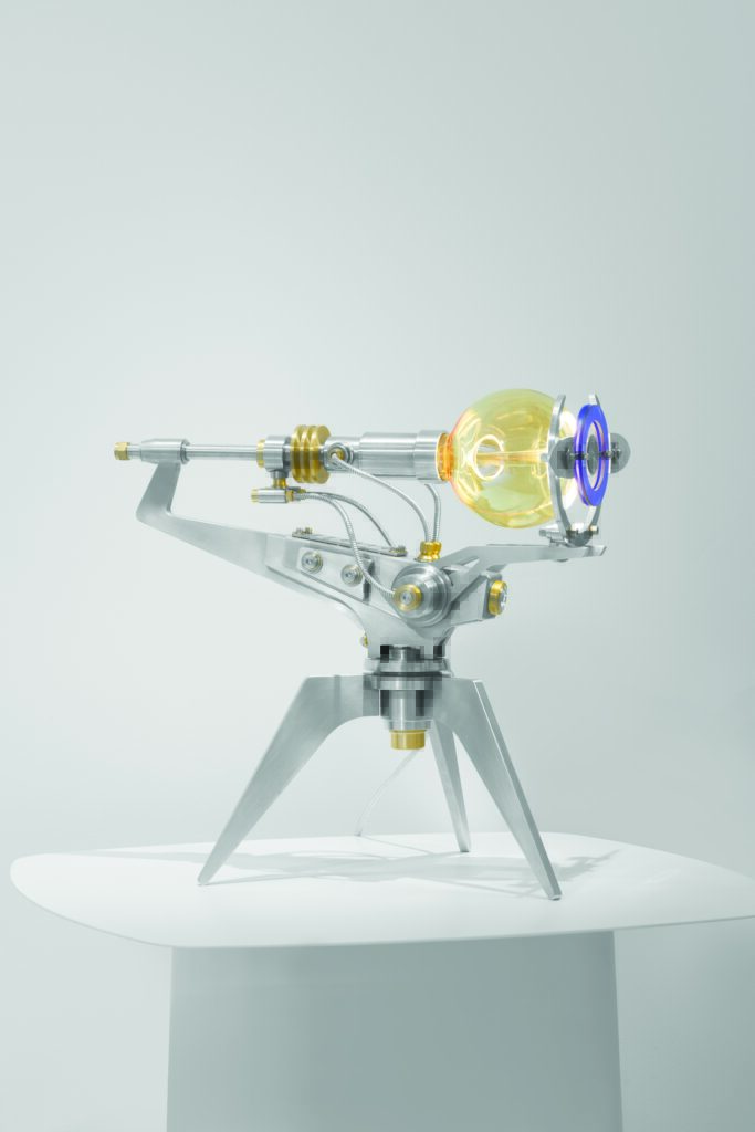 la ML15 Helios, est un soleil mécanique limité à 15 exemplaires. Pesant 9 kg d'acier inoxydable et de laiton, cette sculpture lumineuse arbore une ampoule sphérique entourée d'une couronne solaire et de deux anneaux bleus
