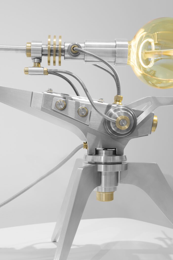 la ML15 Helios, est un soleil mécanique limité à 15 exemplaires. Pesant 9 kg d'acier inoxydable et de laiton, cette sculpture lumineuse arbore une ampoule sphérique entourée d'une couronne solaire et de deux anneaux bleus